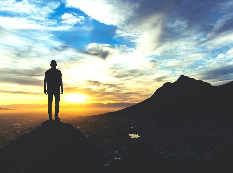 Silhouette of a man standing on a mountain looking at the sunset